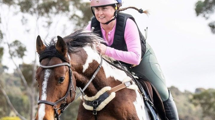 smiling rider jumping her horse in pink base layer and sage riding tights