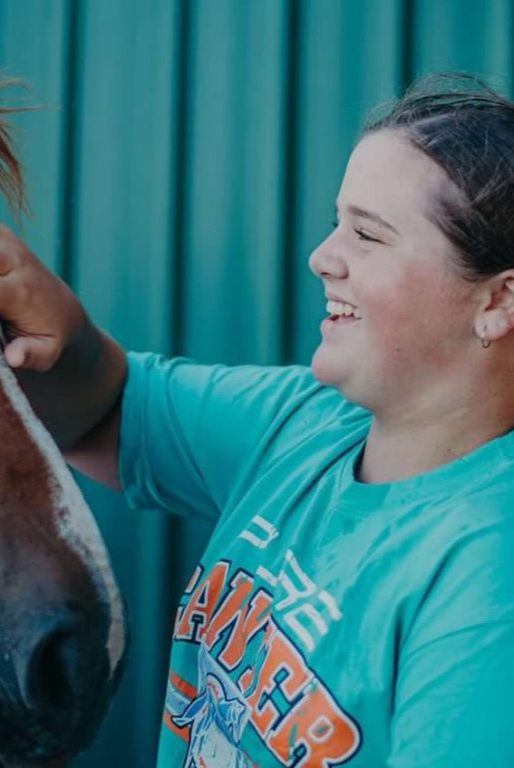 Young girl wearing teal coloured crop top while patting horse