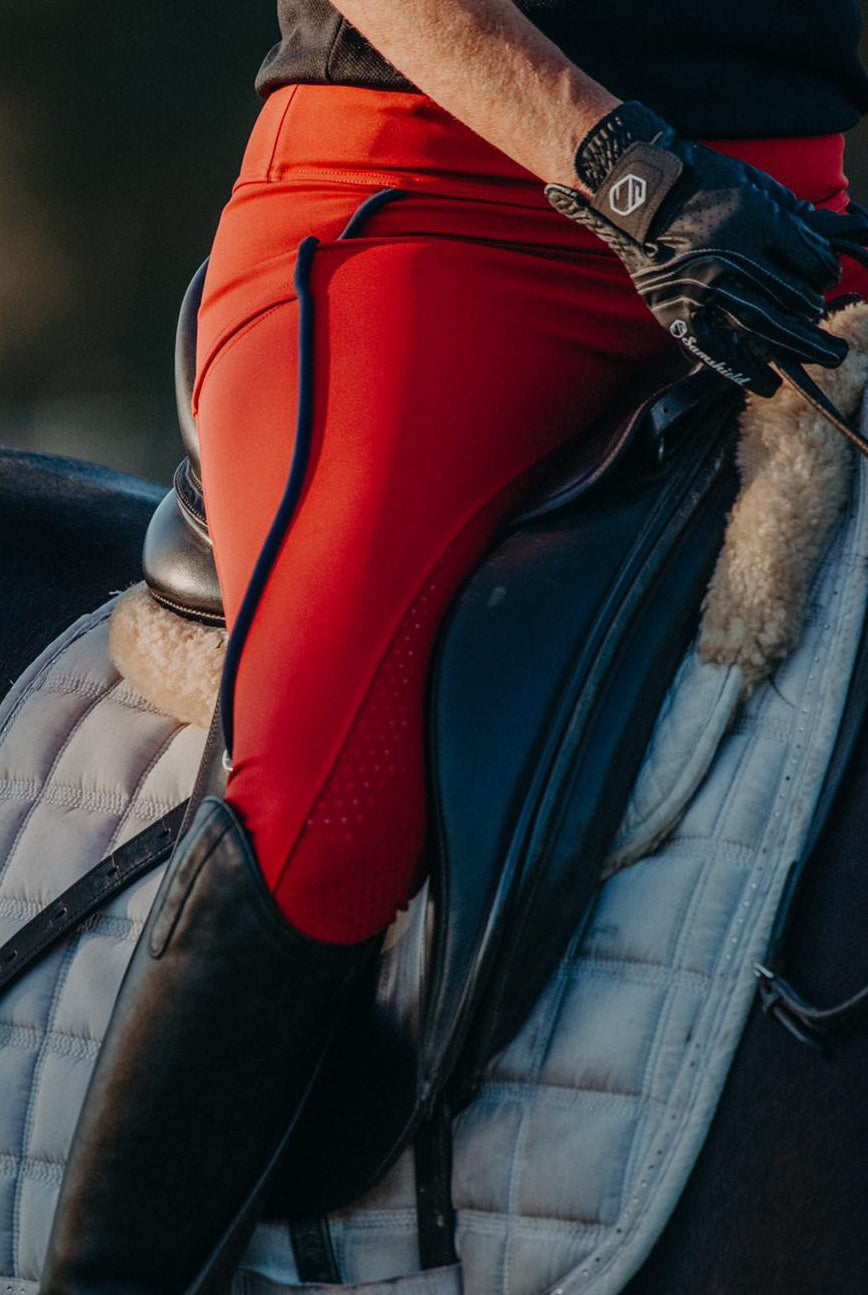 close up leg shot of rider on horse wearing crimson red riding tights with navy trim