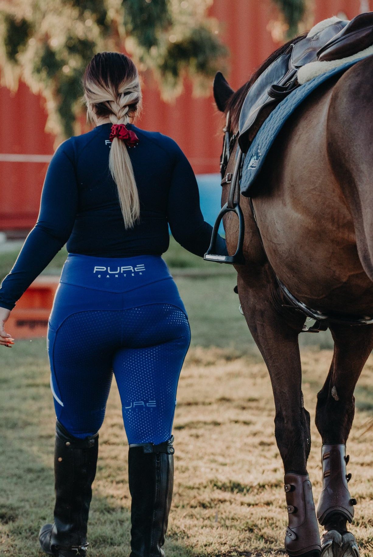Back view of girl leading her horse in royal blue riding tights and navy base layer