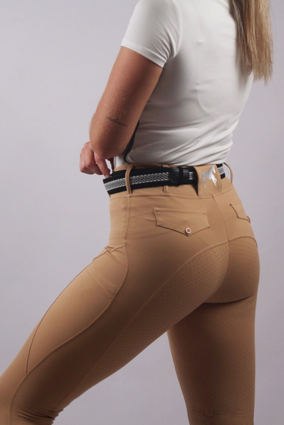 A close-up of a rider's leg in sleek tan riding tights, showcasing a comfortable and flexible fit.