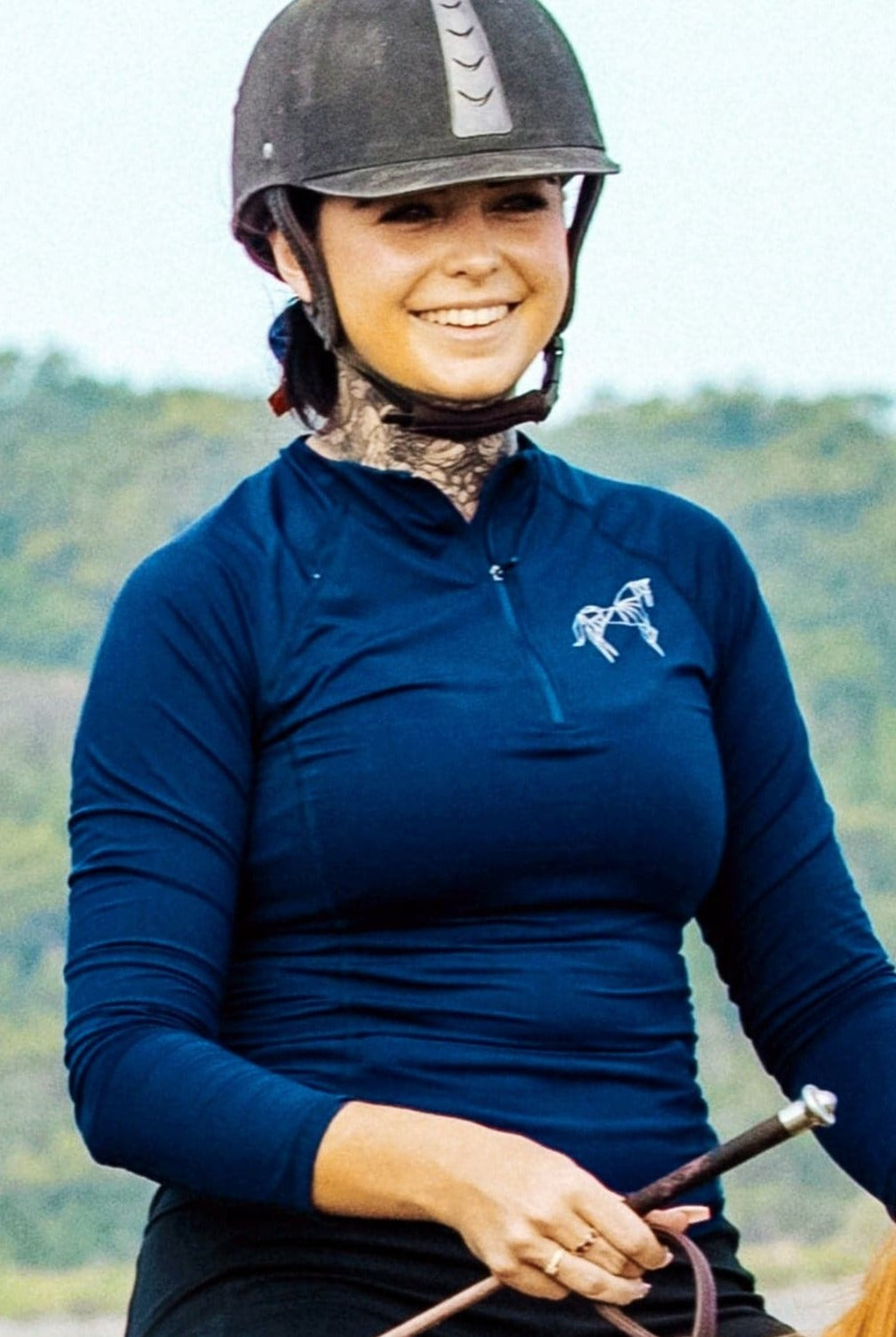 A photo displaying a rider wearing a navy equestrian base layer, featuring built-in sun protection. The UPF-rated fabric shields the rider's skin from harmful UV rays, ensuring a safer and more enjoyable time in the saddle.